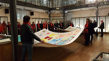 In an interior space, two groups of people are holding two large painted sails and people are looking at them